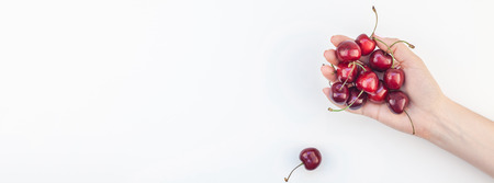 Long wide banner of fresh ripe cherry in a female hands with copy space isolated on white background in minimal style. Concept of summer fun and healthy eating. Template for your text or food designの写真素材