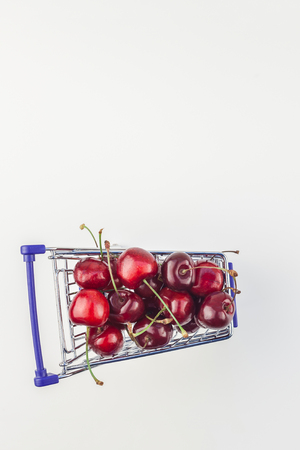 Creative top view of ripe cherries in a shopping cart with copy space isolated on white background in minimal style. Concept of supermarket or fruit market shopping. Template for your text or design.の写真素材
