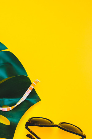 Tropical jungle palm monstera leaves, sunglasses and a woman's swimsuit top on bright yellow paper background. Summer vacations creative flat lay concept template for textの写真素材
