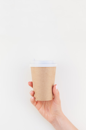 Creative mock up image of woman hand holding craft paper coffee cup with copy space isolated on white background in minimalism style. Template for feminine blog, social mediaの写真素材