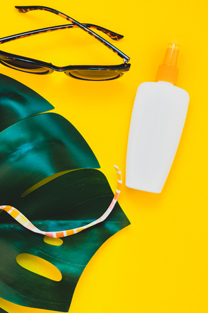 Tropical jungle palm monstera leaves, sunglasses, sunscreen blank bottle mockup and woman's swimsuit top on bright yellow paper background. Summer vacations creative flat lay concept template for textの写真素材