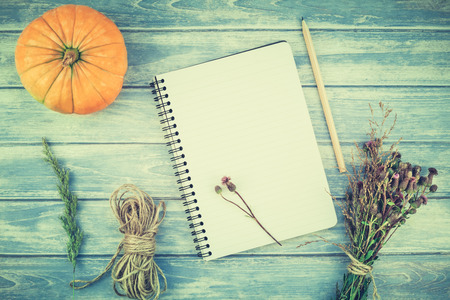 Top view of autumn orange pumpkins and dry flowers with grass thanksgiving background over blue toned wooden table with notebook mock up and copy space in rustic style, template for textの写真素材