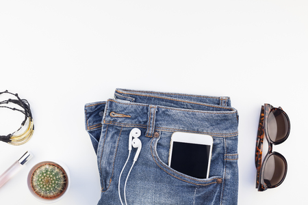 Flat lay of suede shoes, blue jeans, bracelets and smartphone with headphones on white background with copy space. Overhead view of woman casual outfit. Trendy hipster look top viewの写真素材