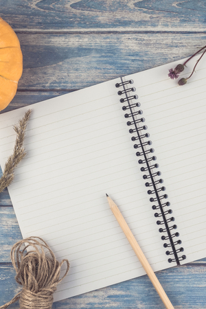 Top view of autumn orange pumpkins and dry flowers with grass thanksgiving background over blue toned wooden table with notebook mock up and copy space in rustic style, template for textの写真素材