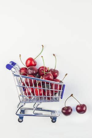 Creative image of ripe cherries in a shopping cart with copy space isolated on white background in minimal style.の写真素材