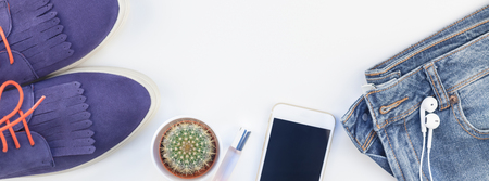 Long wide banner Flat lay of suede shoes, blue jeans, bracelets cactus and smartphone headphones on white background with copy space. Overhead view of woman casual outfit. Trendy hipster look top viewの写真素材