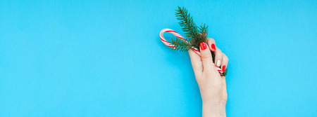 New Year or Christmas top view Xmas holiday celebration woman hand red manicure holding fir branch sweet cane copy space turquoise blue color paper background minimal style. Long wide bannerの写真素材