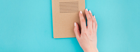 Long wide banner of woman hands holding craft paper notebook diary with copy space on turquoise...