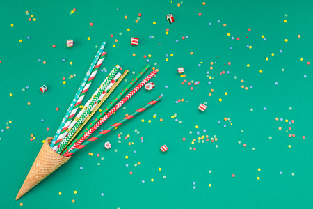 New Year or Christmas pattern flat lay top view Xmas holiday celebration drinking cocktail party straws in waffle cone green paper colourful confetti background. Template for greeting card text designの写真素材