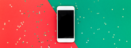Creative New Year or Christmas smartphone mockup flat lay top view Xmas holiday celebration mobile phone on red green paper background. Template mock up long wide banner 2019 2020の写真素材