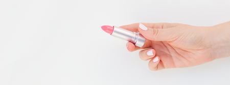 Woman hand with pastel manicure polish holding pink lipstick isolated on white background with copy space. Long wide banner for feminine beauty blog social mediaの写真素材