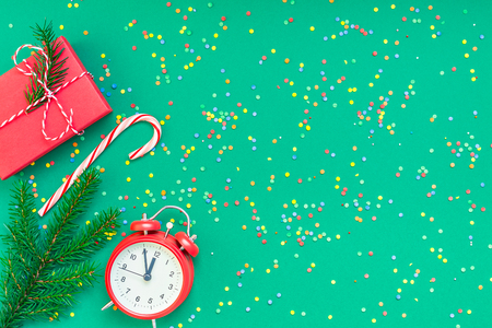 New Year or Christmas pattern flat lay top view with red alarm clock twelve midnight fir tree branch Xmas holiday celebration green paper bright colorful confetti background.の写真素材