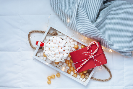 New Year or Christmas flat lay top view with Hot cacao coffee chocolate with marshmallows mug Xmas holiday celebration red present box on wooden tray in bed with lights. Concept blog social media 2019の写真素材