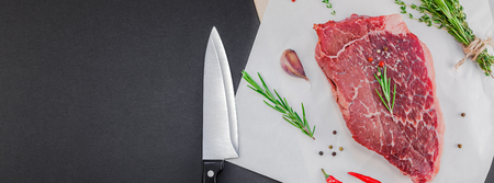 Creative Top view flat lay of fresh raw beef meat striploin steak with rosemary thyme herbs garlic pepper mushrooms black background with copy space. Food preparation cooking concept Long wide bannerの写真素材