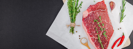 Creative Top view flat lay of fresh raw beef meat striploin steak with rosemary thyme herbs garlic pepper mushrooms black background with copy space. Food preparation cooking concept Long wide bannerの写真素材