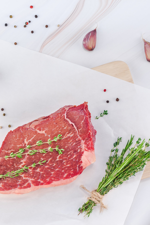 Creative Top view flat lay of fresh raw beef meat striploin steak with rosemary thyme herbs garlic pepper mushrooms on white marble table background with copy space. Food preparation cooking conceptの写真素材
