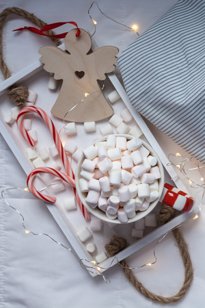 New Year or Christmas flat lay top view with Hot cacao coffee chocolate with marshmallows mug Xmas holiday celebration on wooden tray in bed with lights. Concept blog social media 2019の写真素材
