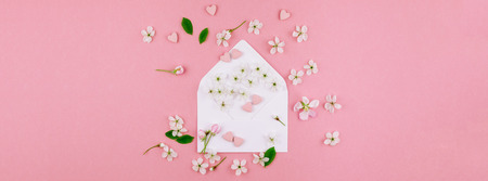 Creative flat lay long wide banner of blank letter envelope, spring flowers and hearts candies on millennial pink background with copy space in minimal style, template for valentine cardsの写真素材
