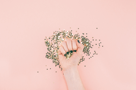 New Year or Christmas Top view of woman hands black manicure covered golden stars confetti with copy space millennial pink color paper background minimal style. Template for feminine blog social mediaの写真素材