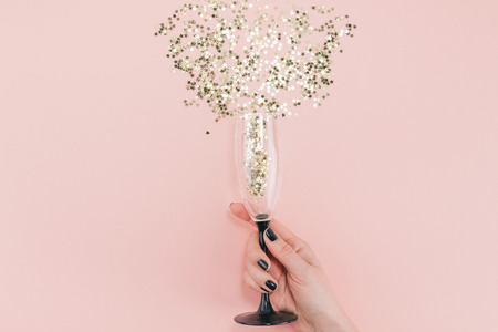 New Year Christmas Top view flat lay champagne glass poured out golden stars confetti woman hand black manicure millennial pink color paper background minimal style Template feminine blog social mediaの写真素材