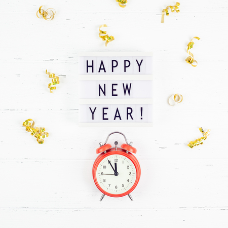 New Year or Christmas pattern flat lay top view red alarm clock twelve midnight Xmas holiday celebration white wooden golden sparkles confetti background. Template for your text design 2019の写真素材