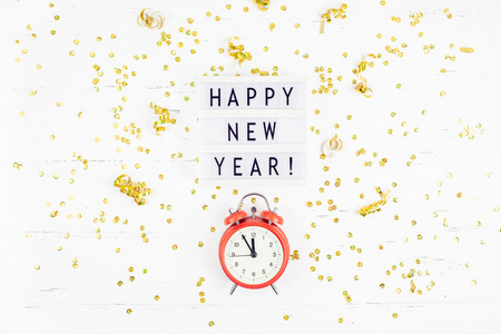 New Year or Christmas pattern flat lay top view red alarm clock twelve midnight Xmas holiday celebration white wooden golden sparkles confetti background. Template for your text design 2019の写真素材