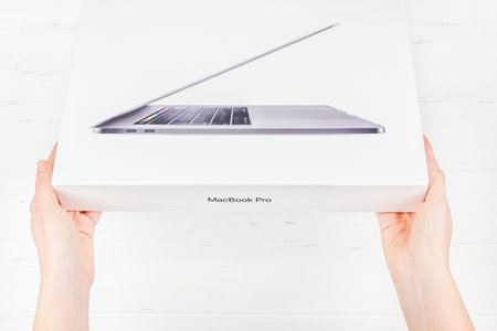 BERLIN, GERMANY - DECEMBER 09, 2018: Woman hands holding the box of the latest Apple Macbook Pro laptop computer against white wooden background. Unboxing top view concept with copy spaceのeditorial素材