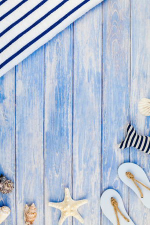 Creative flat lay concept of summer travel vacations. Top view of towel flip flops seashells and starfish on pastel blue wooden planks background with copy space in rustic style frame template textの写真素材
