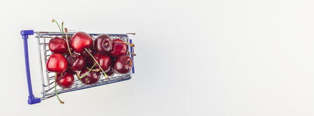 Long wide banner of ripe cherries in a shopping cart with copy space isolated on white background in minimal style. Concept of supermarket or fruit market shopping. Template for your text or design.の写真素材