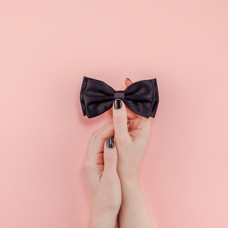 Creative flatlay top view retro black bow tie woman hands black manicure pink paper background copy space.の写真素材