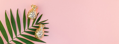 Creative flat lay top view of green tropical palm leaves millennial pink paper background with pineapples copy space. Minimal tropical palm leaf plants summer concept template for your text or designの写真素材