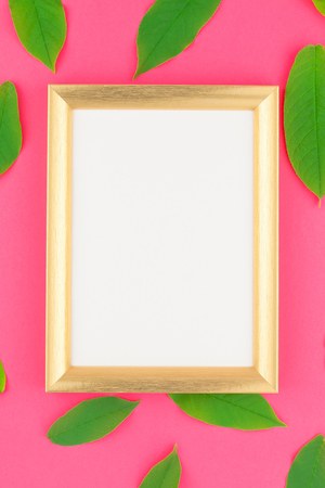 Creative flat lay top view pattern with fresh green leaves on bright pink background with golden frame mock up and copy space in minimal pop art style, template for textの写真素材