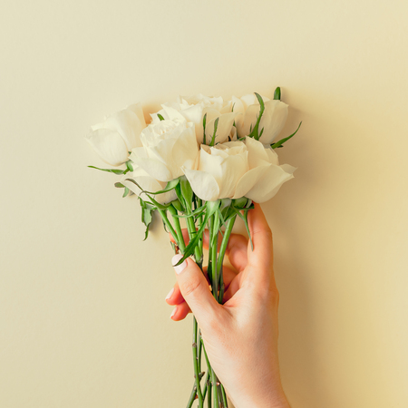 Creative top view flat lay woman hands holding fresh white roses bouquet with copy space pastel paper background minimalism style. Template feminine blog social media holiday wedding invitation cardの写真素材