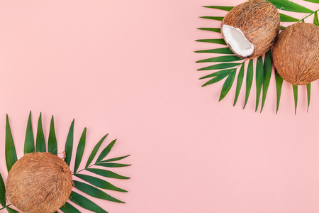 Creative flat lay top view of green tropical palm leaves coconut fruits and coconut oil cosmetics for skin and hair care on pink paper background copy space. Minimal tropical summer beauty spa conceptの写真素材