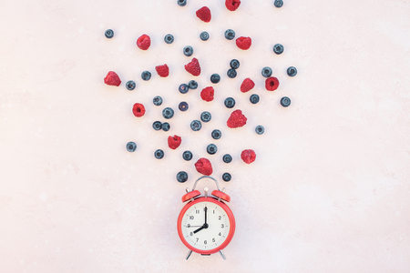 Creative concept composition flat lay top view red alarm clock raspberry blueberry pink background copy space Template greeting card text social media blogsの写真素材