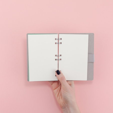 Creative flat lay top view of woman hands black manicure with empty notebook mock up on pastel millennial pink paper background copy space. Minimal writing concept template for text lettering bloggingの写真素材