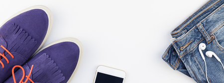 Long wide banner Flat lay of suede shoes, blue jeans, bracelets and smartphone with headphones on white background with copy space. Overhead view of woman casual outfit. Trendy hipster look top viewの写真素材