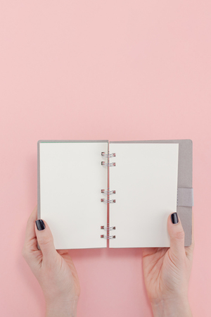 Creative flat lay top view of woman hands black manicure with empty notebook mock up on pastel millennial pink paper background copy space. Minimal writing concept template for text lettering bloggingの写真素材
