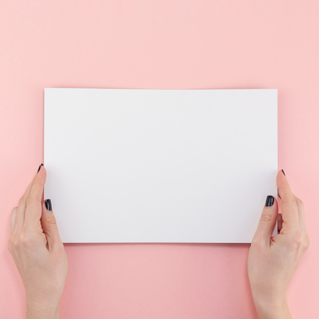 Creative flat lay top view of woman hands black manicure with empty A4 paper page mock up on pastel millennial pink paper background copy space. Minimal writing concept template for text lettering bloggingの写真素材