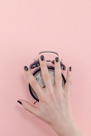 Creative flat lay morning time emotions concept top view of woman hand holding black vintage alarm clock pastel millennial pink color paper background with copy space minimal style template for textの写真素材
