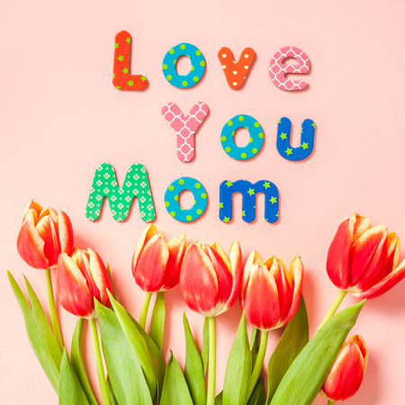 Creative flat lay top view Mothers Day greeting card with red tulips spring flowers on pink background. Celebration Postcard templateの写真素材