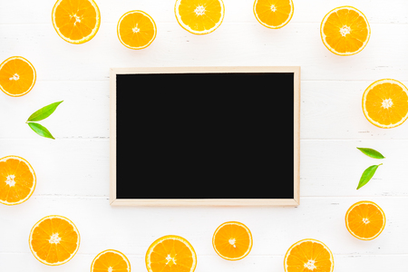 Creative scandinavian style flat lay top view of fresh orange fruit slices on white wooden table background with blackboard frame mockup. Minimal summer fresh citrus pattern for blog or recipe bookの写真素材