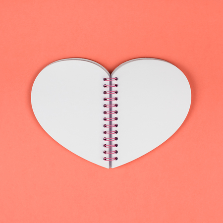 Creative top view flat lay of heart shaped notepad with blank pages as mockup with copy space on coral color paper background minimal style. Template for feminine blog social media, valentine postcardの写真素材