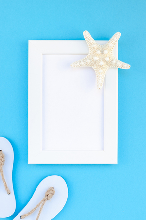 Creative flat lay concept of summer travel vacations. Top view of seashells and starfish on turquoise blue background with white frame mock up and copy space in minimal style, template for textの写真素材