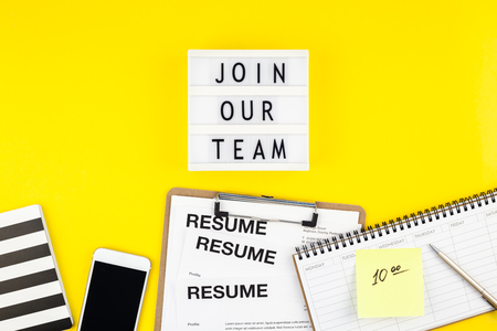 Creative top view flat lay of desk with join our team text on lightbox copy space on bold yellow background in minimal style. Concept of new job, hiring recruitment process, new team members screening