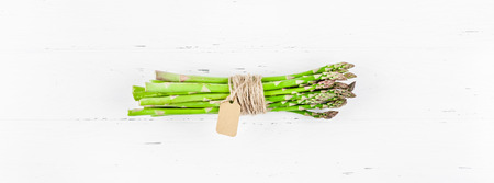Creative scandinavian style flat lay top view mockup of fresh green asparagus on white wooden table background copy space. Minimal house cooking concept mock up for blog or recipe bookの写真素材