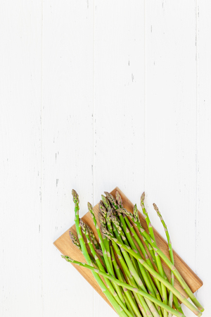 Creative scandinavian style flat lay top view mockup of fresh green asparagus on white wooden table background copy space. Minimal house cooking concept mock up for blog or recipe bookの写真素材