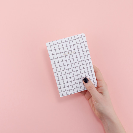 Top view of woman hand with stylish black manicure holding notepad with copy space on pink color...