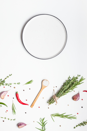 Flat lay overhead view empty plate mockup blank text space invitation card on white background with greens herbs and spices. Menu design food background with cooking ingredientsの写真素材