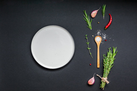 Flat lay overhead view empty plate mockup blank text space invitation card on black background with greens herbs and spices. Menu design food background with cooking ingredientsの写真素材
